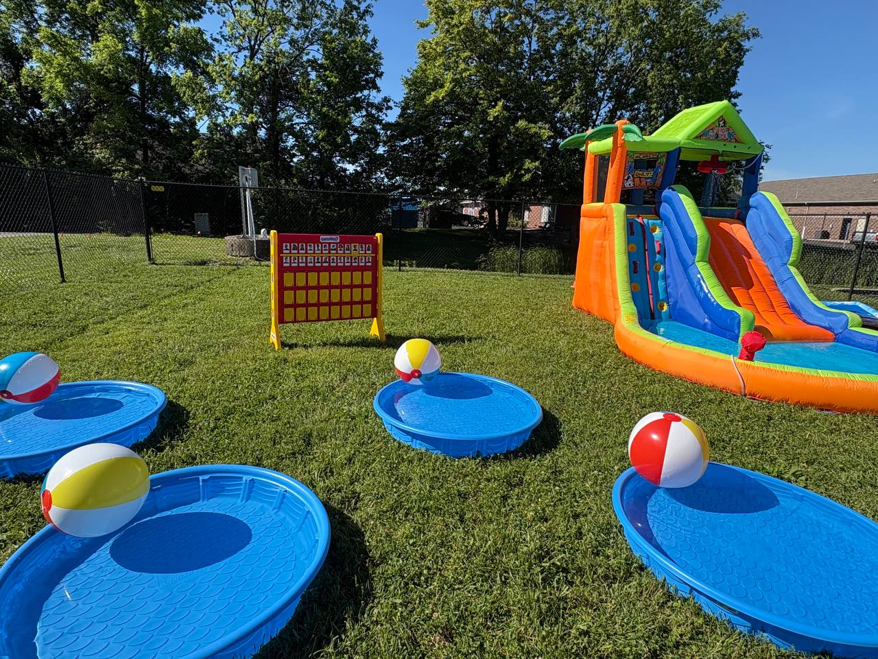 Backyard party setup with inflatable slide, kiddie pools, beach balls, and yard games