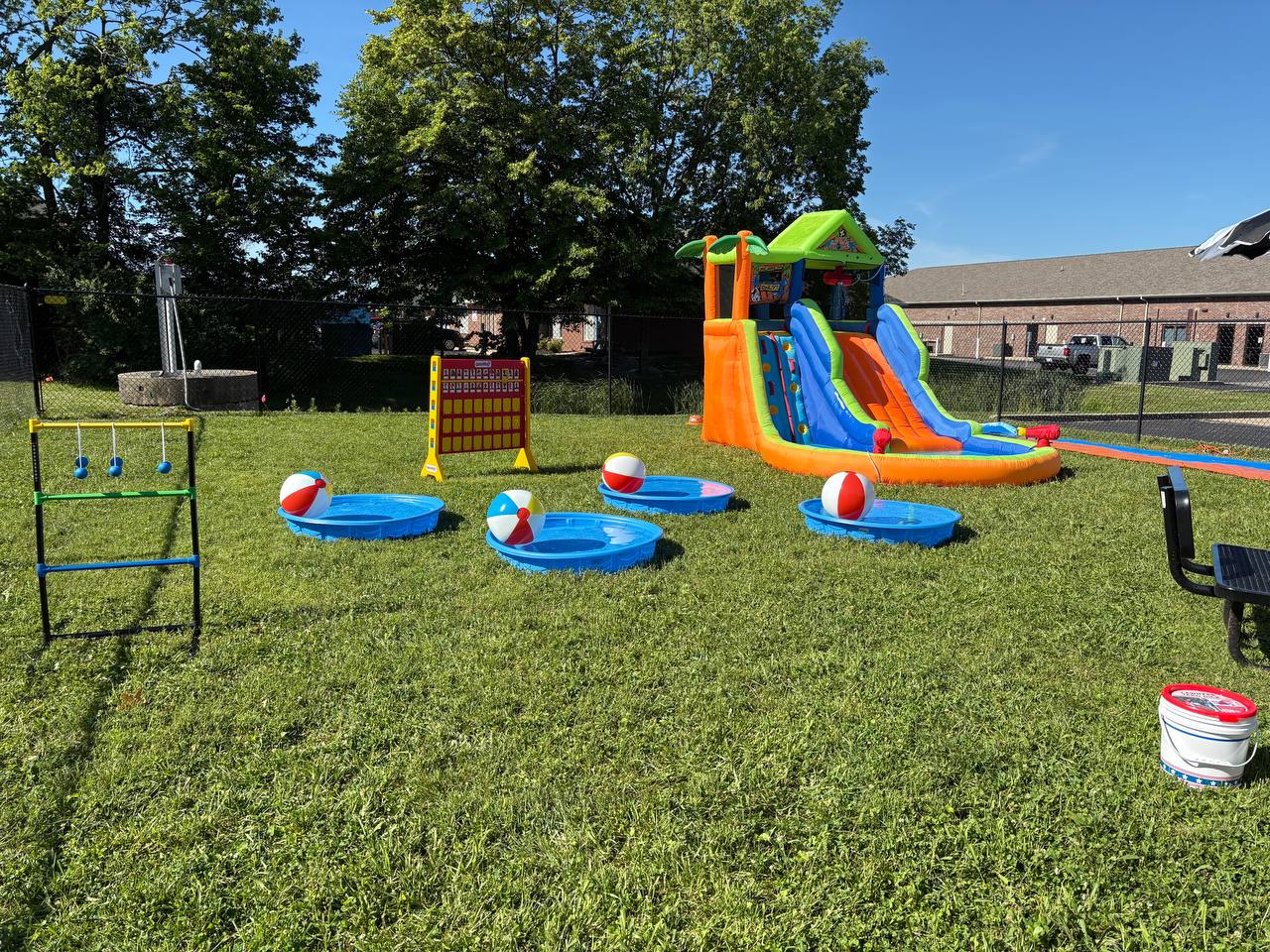 Outdoor party setup with yard games, pools, inflatable slide, and shaded seating
